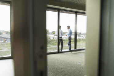 Two young businessmen standing on balcony talking - UUF005473