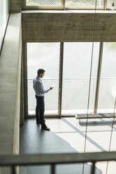 Young businessman looking on cell phone at the window - UUF005480