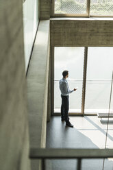 Young businessman with cell phone looking out of window - UUF005481