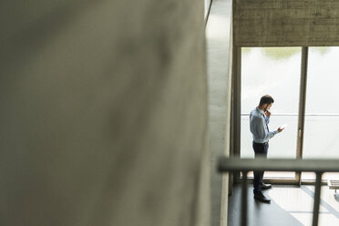 Young businessman looking on cell phone at the window - UUF005482