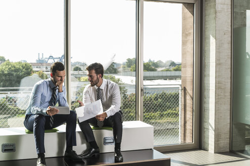 Zwei junge Geschäftsleute betrachten ein Dokument und ein digitales Tablet - UUF005549