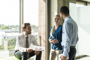 Drei lächelnde junge Geschäftsleute diskutieren über ein Dokument - UUF005492