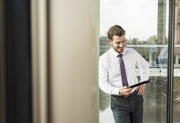 Smiling young businessman looking at digital tablet - UUF005524