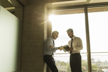 Two young businessmen talking at the window in office - UUF005551
