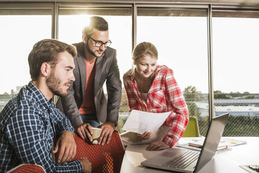 Three young people in conference room looking at laptop - UUF005548