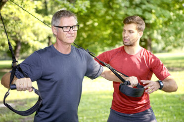 Mann beim TRX-Training, während sein Personal Trainer ihn beobachtet - SEGF000416