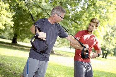 Mann beim TRX-Training, während sein Personal Trainer ihn beobachtet - SEGF000399