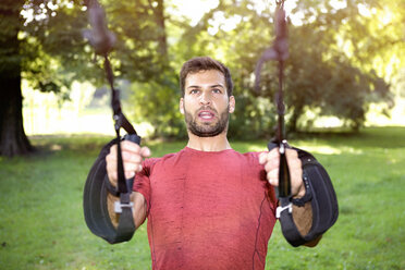 Portrait of sportive man doing TRX training in a park - SEGF000400