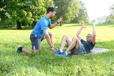 Mann beim Krafttraining auf einer Wiese, während sein Personal Trainer ihn beobachtet - SEGF000418