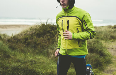 Spanien, Valdovino, junger Mann beim Joggen am Strand an einem regnerischen Tag - RAEF000387