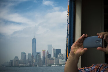 USA, New York City, Tourist taking picture with smart phone with view of Manhattan skyline and East River - ONF000889