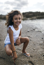 Spanien, Gijon, Porträt eines lächelnden kleinen Mädchens, das am Strand hockt - MGOF000537