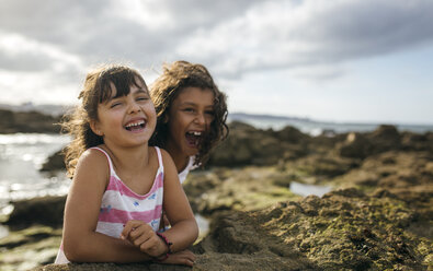 Spain, Gijon, portrait of two laughing little girls at rocky coast - MGOF000550