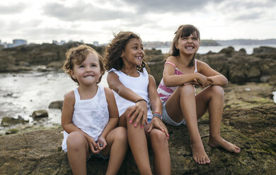 Spain, Gijon, group picture of three little girls sitting at rocky coast - MGOF000562