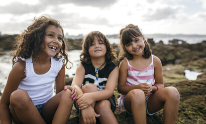 Spain, Gijon, group picture of three little children sitting at rocky coast - MGOF000552