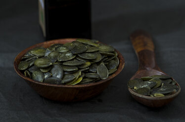 Wooden bowl and spoon of pumpkin seeds on dark ground - ODF001226