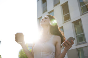 Frau hört Musik vom Smartphone und hält eine Kaffeetasse - FMKYF000621