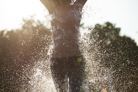 Frau läuft durch einen Springbrunnen und verspritzt Wassertropfen, lizenzfreies Stockfoto