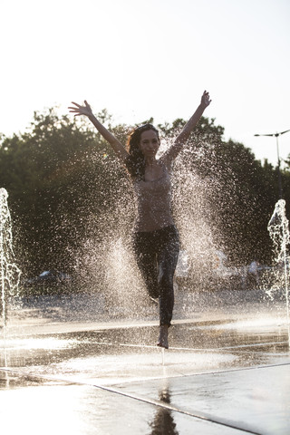 Frau läuft durch einen Springbrunnen und verspritzt Wassertropfen, lizenzfreies Stockfoto