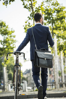 Junger Geschäftsmann, der ein Fahrrad schiebt und ein Smartphone in der Hand hält - UUF005566