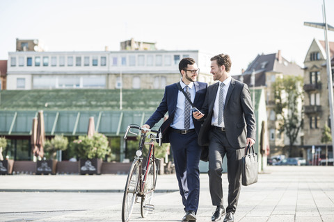 Zwei Geschäftsleute mit Fahrrad und Smartphone beim Spaziergang in der Stadt, lizenzfreies Stockfoto