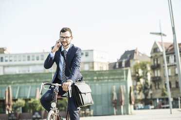 Young businessman riding bicycle, talking on the phone - UUF005573