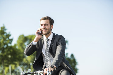 Young businessman riding bicycle, talking on the phone - UUF005576