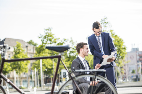 Zwei junge Geschäftsleute besprechen Akten im Freien, lizenzfreies Stockfoto