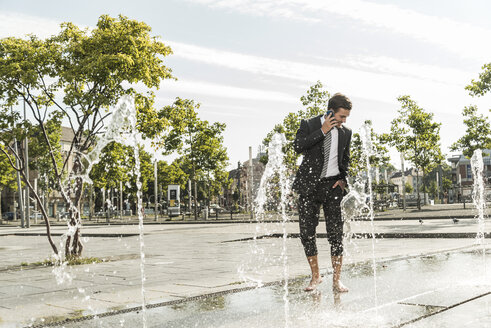 Junger Geschäftsmann steht im Brunnen und telefoniert - UUF005592