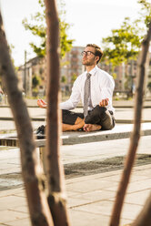 Young businessman meditating on bench - UUF005599