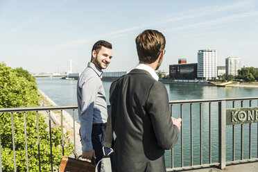 Zwei junge Geschäftskollegen, die am Fluss spazieren gehen und sich unterhalten - UUF005602