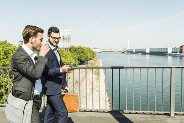 Two young business colleagues walking by river, discussing - UUF005604