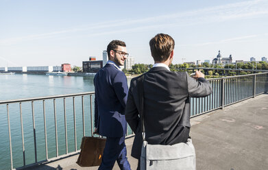 Zwei junge Geschäftskollegen, die am Fluss spazieren gehen und sich unterhalten - UUF005605