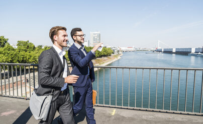 Zwei junge Geschäftskollegen, die am Fluss spazieren gehen und sich unterhalten - UUF005606