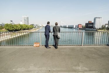 Young businessmen standing at railing looking at river - UUF005607