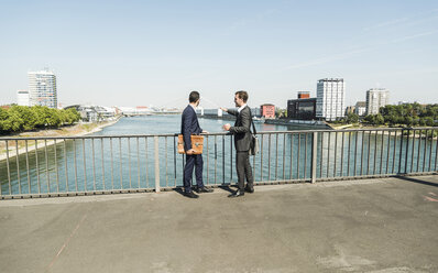 Young businessmen standing at railing looking at river - UUF005609