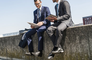 Zwei junge Geschäftsleute sitzen an einer Mauer am Fluss und arbeiten - UUF005619
