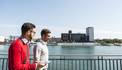 Two young businessmen walking by the riverside - UUF005624