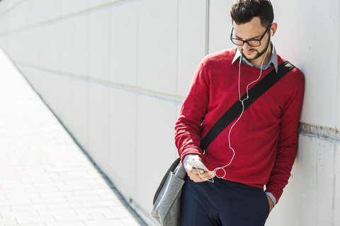 Junger Geschäftsmann, der ein Smartphone benutzt und Kopfhörer trägt, lizenzfreies Stockfoto