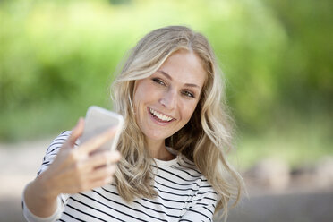 Porträt einer glücklichen blonden Frau, die ein Selfie mit ihrem Smartphone macht - FMKF001996