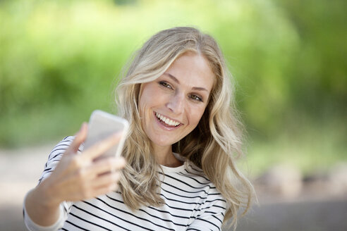 Porträt einer glücklichen blonden Frau, die ein Selfie mit ihrem Smartphone macht - FMKF001996