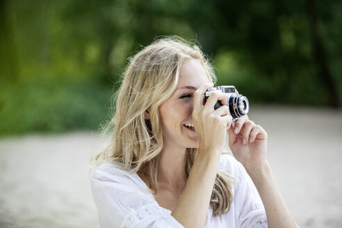 Lächelnde blonde Frau, die ein Foto mit einer alten Kamera macht - FMKF002066