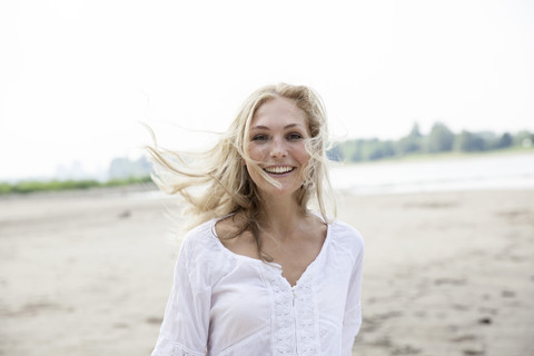 Porträt einer lächelnden blonden Frau mit wehendem Haar am Strand, lizenzfreies Stockfoto