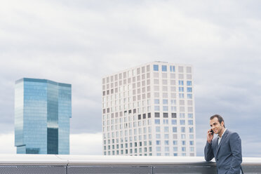 Geschäftsmann auf städtischem Balkon, der mit einem Handy telefoniert - BZF000216