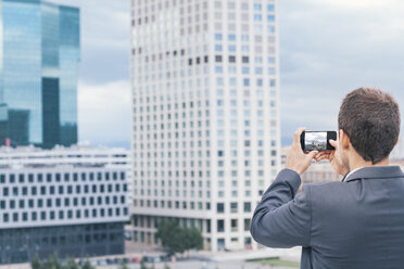 Businessman taking cell phone photograph at city buildings - BZF000226