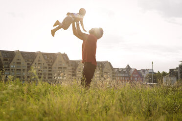 Germany, Cologne, father lifting up his son in a field - MADF000630