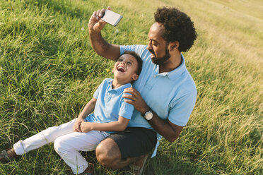 Vater und glücklicher Sohn auf einem Feld, der ein Selfie macht - MADF000653
