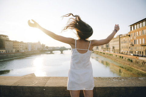 Italy, Florence, back view of happy woman wearing white summer dress standing on a bridge at sunset stock photo