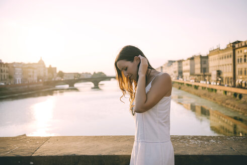 Italien, Florenz, glückliche Frau in weißem Sommerkleid steht auf einer Brücke bei Sonnenuntergang - GEMF000327