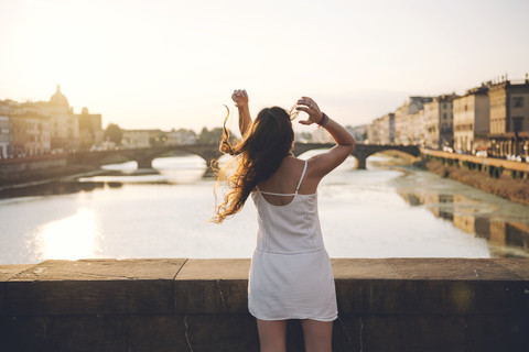 Italien, Florenz, Rückenansicht einer Frau im weißen Sommerkleid auf einer Brücke bei Sonnenuntergang, lizenzfreies Stockfoto